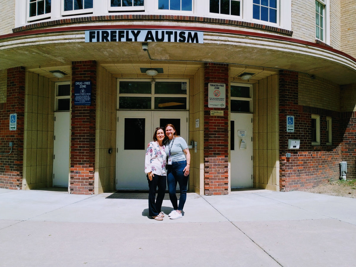 Two women standing in front of a building with 'Firefly Autism' sign.