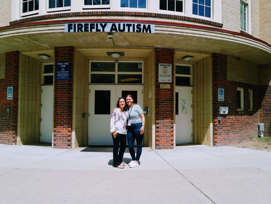 Two women standing in front of a building with 'Firefly Autism' sign.